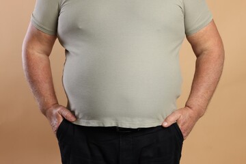 Overweight man in tight t-shirt on beige background, closeup