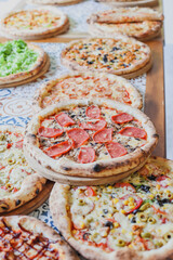 Hot tasty traditional various italian pizzas with salami, meat, cheese, onion, mushroom, tomatoes greens on a dark background