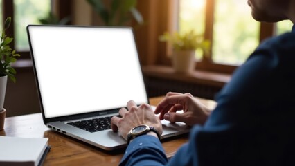 A person is shown working on a laptop with a blank white screen at a wooden desk. Concept of: Remote work and digital workspace.