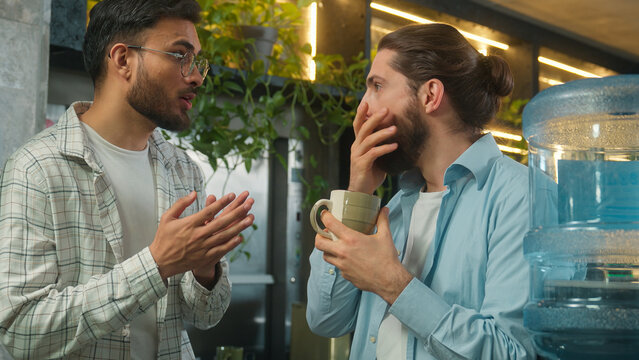 Male colleagues friends buddies multiethnic men business partners coworkers Arabian Caucasian guys businessmen freelancers talk laugh gossip friendly conversation in break zone office coworking cafe