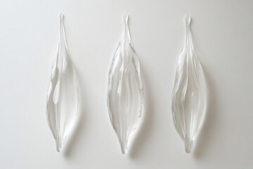 Three translucent, teardrop-shaped glass sculptures arranged symmetrically against a white...