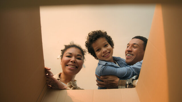 POV point of view open cardboard box looking inside African American happy family joyful parents son kid little boy child unpacking parcel delivery online shop receive package unboxing moving day home