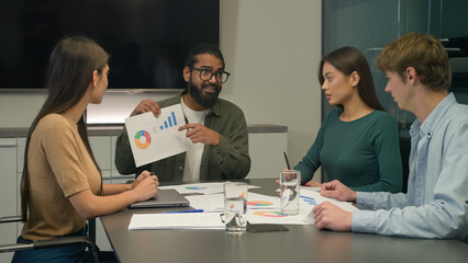 Arabian businessman talk to team employees pointing to graph report business presentation group multiracial workers men women male female listen team leader at conference table office meeting briefing