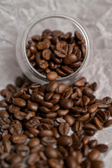 Fresh aromatic roasted coffee beans spilled from a small glass on craft paper. Arabica and robusta blend