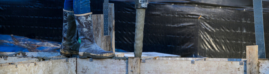 Construction worker walking on wood cement form panels for foundation walls guiding concrete boom...