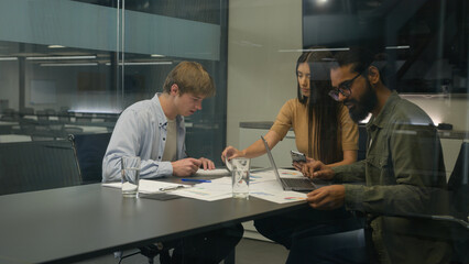 Group of coworkers woman men colleagues managers diverse businesswoman businessmen sit at table office boardroom team work with devices analyzing corporate business project graphs documents in company