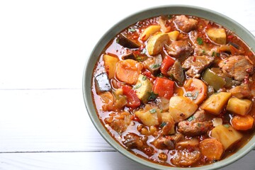 Delicious stew with vegetables in bowl on white wooden table, closeup