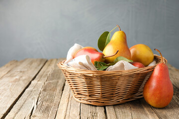 Ripe juicy pears in wicker basket on wooden table against grey background