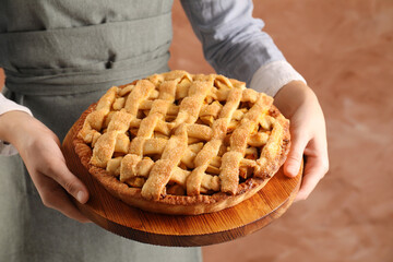 Woman holding wooden board with tasty homemade apple pie on light coral background, closeup