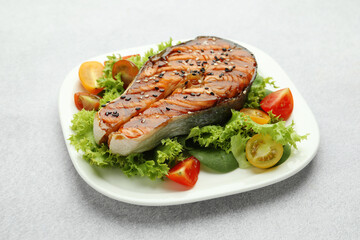 Tasty grilled salmon steak and vegetables on light grey table, closeup