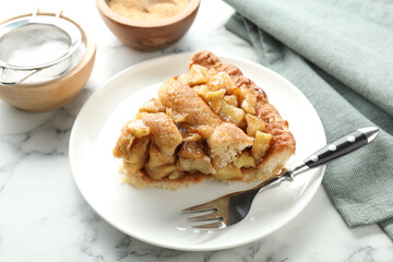 Slice of homemade apple pie and fork on white marble table