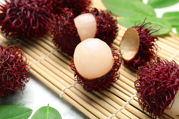 Delicious ripe rambutans and green leaves on white marble table, closeup