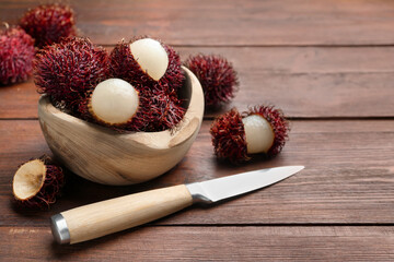Delicious ripe rambutans in bowl and knife on wooden table, space for text
