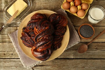 Tasty buns with poppy seeds and ingredients on wooden table, flat lay
