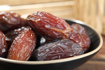 Many tasty dried dates in bowl on table, closeup