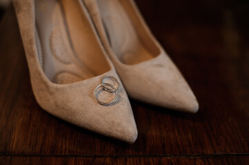 Elegant Wedding Shoes with Silver Rings on a Wooden Table