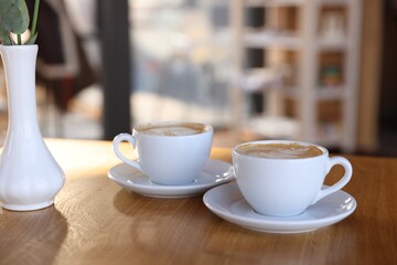 Cups of aromatic coffee on wooden table in cafe, closeup