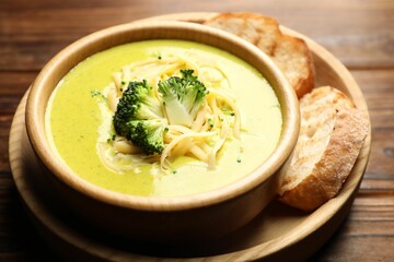Delicious broccoli cream soup in bowl and croutons on wooden table, closeup