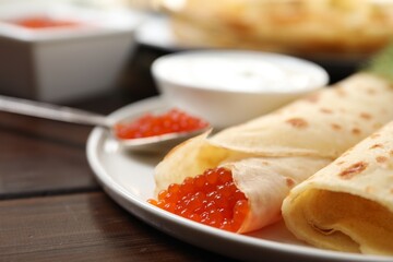 Delicious crepes with red caviar served on wooden table, closeup