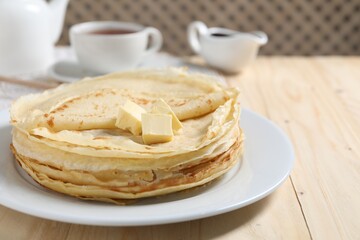Stack of tasty crepes with butter on wooden table, closeup