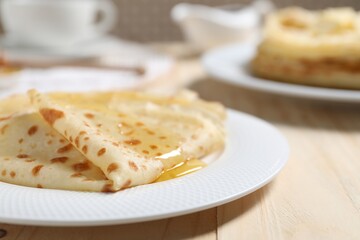 Tasty crepes with honey on wooden table, closeup