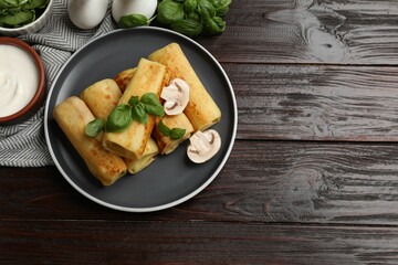 Delicious rolled crepes with mushrooms, basil and sour cream on wooden table, flat lay. Space for text