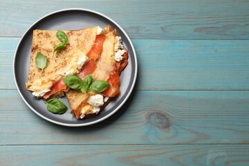 Delicious crepes with salmon, cream cheese and basil on light blue wooden table, top view. Space for text