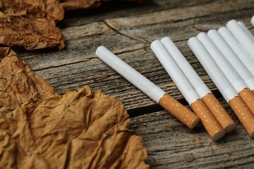 Dried tobacco leaves and cigarettes on wooden table, closeup