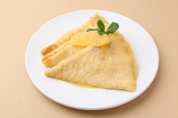 Plate with tasty crepes Suzette on beige table, closeup