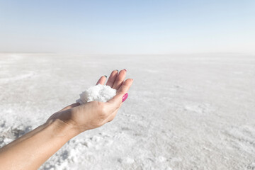 Woman hand holding snowflakes or salt frozen lake background. Global Warming Climate Change and Concept. end of the world. salt lake surface, dry salt lake