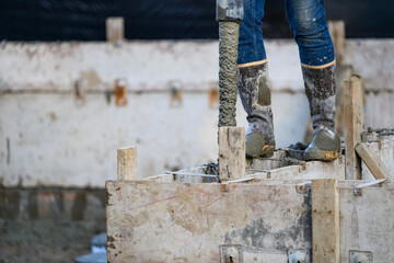 Construction worker walking on wood cement form panels for foundation walls guiding concrete boom pump truck pipe into forms, winter house building project job site
