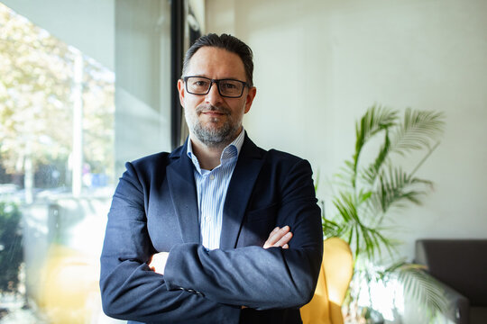 Portrait of a confident businessman standing by a window in modern office