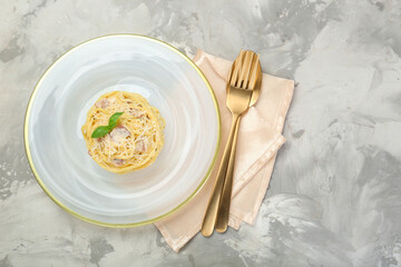 Plate with delicious pasta Carbonara and cutlery on grey textured table, top view