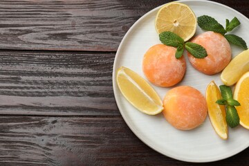 Plate with tasty mochi, cut orange, lemon and mint on wooden table, top view. Space for text