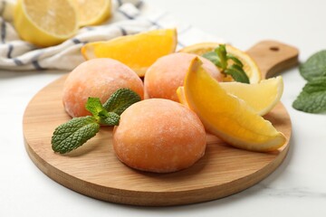 Board with tasty mochi, cut orange and mint on white table, closeup