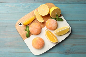 Board with tasty mochi, cut orange, lemon and mint on light blue wooden table, top view