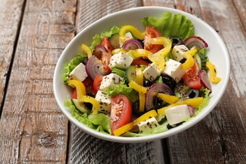 Delicious fresh Greek salad in bowl on wooden table, closeup