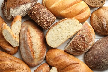 Whole and cut bread loafs on white wooden table, flat lay