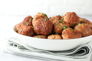Tasty cooked meatballs with green onion in bowl on white table, closeup