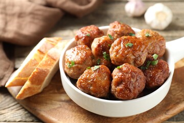 Tasty meatballs with green onion in baking dish and bread pieces on wooden table, closeup