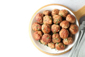 Tasty cooked meatballs with green onion in bowl on white table, top view. Space for text