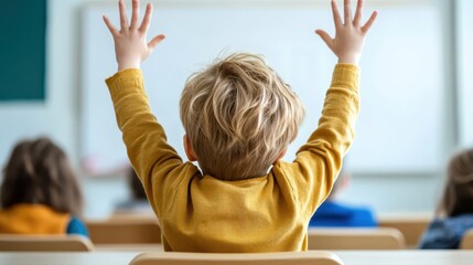 A young boy in a yellow sweater energetically raises his hands high in a classroom, eager to answer or participate, surrounded by other students in the learning environment.