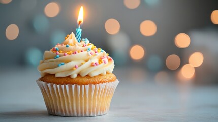 A decorated cupcake with a candle and colorful sprinkles, set against a blurred background.
