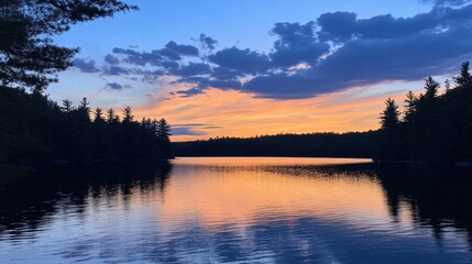 Obraz premium Serene sunset over a calm lake surrounded by trees.