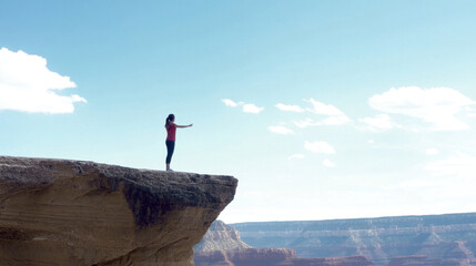 Fototapeta premium Be strong, A person stands on a cliff, arms outstretched, overlooking a vast canyon under a clear blue sky, evoking a sense of freedom and adventure.