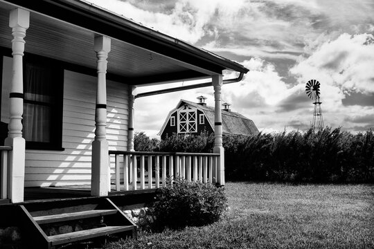 A black and white photo of a house with a porch and a windmill in the background