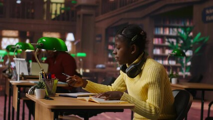 Young focused scholar doing her homework at a library desk after classes, engrossed in literature and notes. Pupil completing her notes in the copybook, productive study sessions. Camera B. - Powered by Adobe