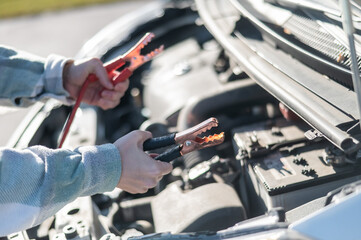 Woman holding clamps for charging a car battery. 