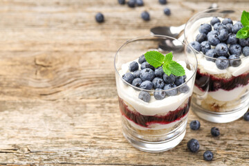 Tasty trifle dessert. Sponge cake, blueberries, jam and whipped cream in glasses on wooden table, closeup. Space for text