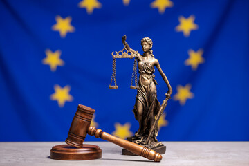 Figure of Lady Justice and judge's gavel on table against European Union flag